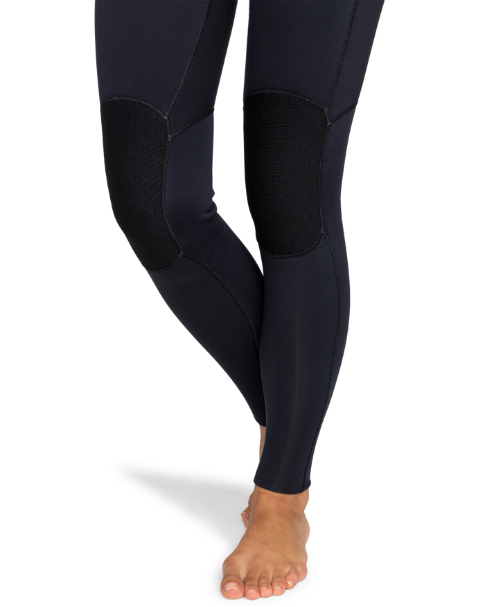 A person wearing the Roxy 3/2mm Swell Chest Zip Fullsuit stands barefoot on a white background, with legs crossed at the ankles.
