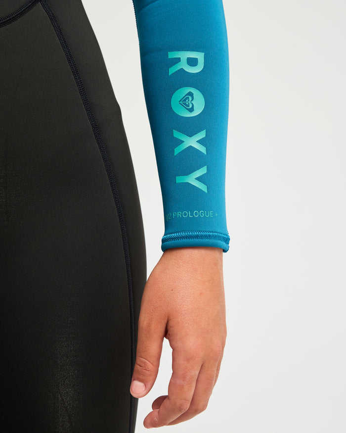 A person’s arm is shown wearing the Roxy 3/mm Prologue Back Zip (Flatlock) Wetsuit, featuring a blue sleeve with “ROXY” and a small teal logo. The wetsuit’s body is black, and the hand rests relaxed by their side against a plain light background.