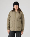 A woman wearing a black beanie, dark pants, and the Roxy Aurora Quilted Bomber in dusky green stands facing the camera against a plain light background.