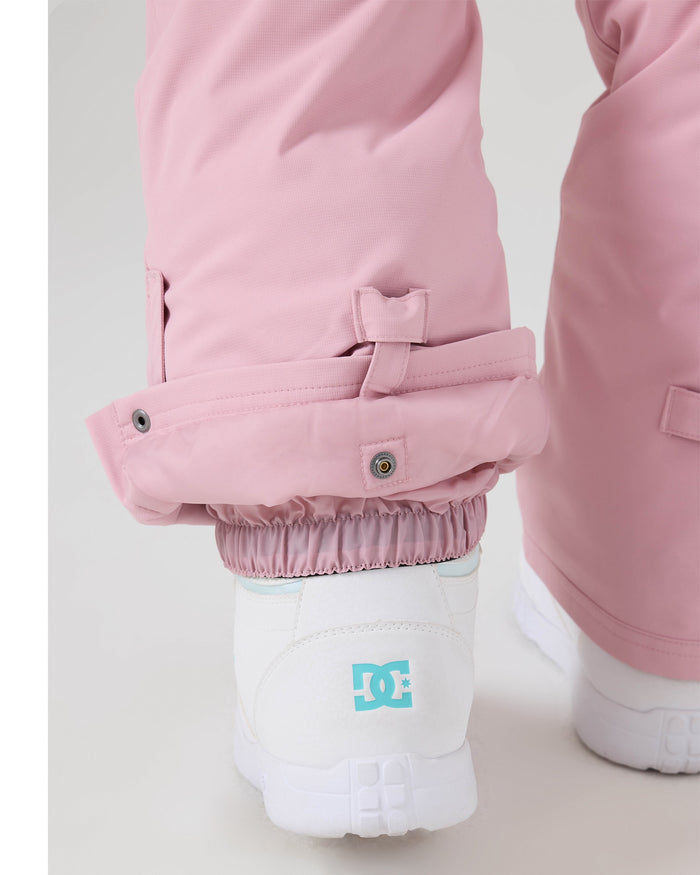 Close-up of a person wearing light pink Roxy Backyard Pants with adjustable cuffs over white sneakers, highlighting the elastic and snap closure details. These waterproof women’s ski pants are crafted from recycled polyester for both style and sustainability.