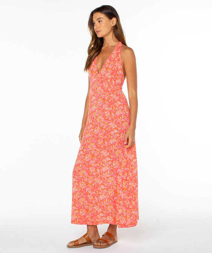 A woman in profile wears the Roxy Beach Day Maxi Dress, a sleeveless style with pink and orange florals, a deep V-neckline, and brown sandals, posed against a plain white background.