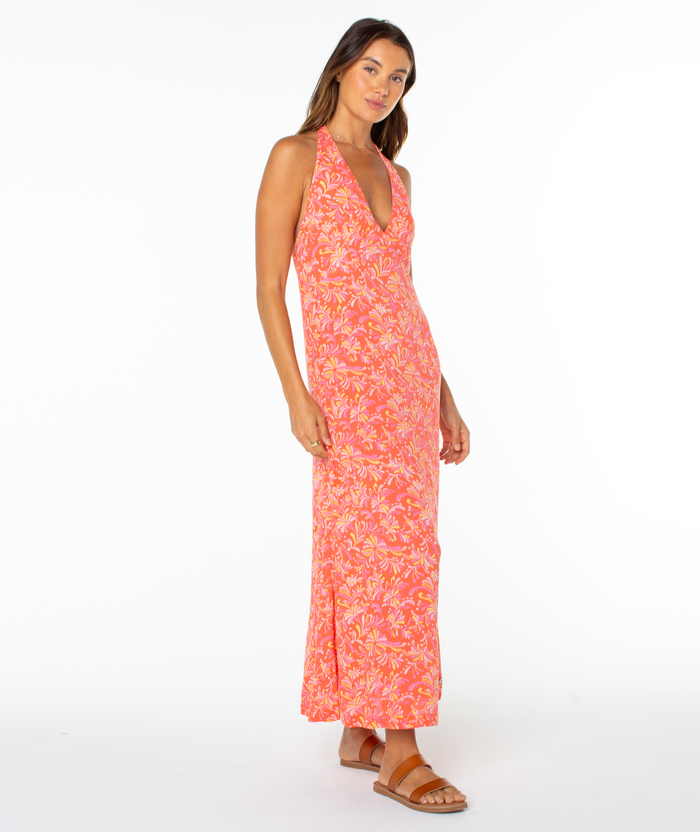 A woman wears the Roxy Beach Day Maxi Dress with a sleeveless halter neckline and pink and yellow florals, paired with brown sandals, standing against a plain white background.