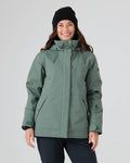 A smiling person wears the Roxy Billie Jacket in Duck Green, paired with black pants and a black beanie, standing against a plain light background.