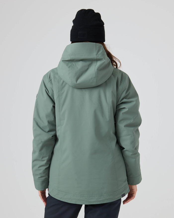 A person wearing the Roxy Billie Jacket—a light green women’s snowboard jacket made from recycled polyester with 10K/5K microripstop fabric—and a black beanie is standing with their back to the camera against a plain light background.