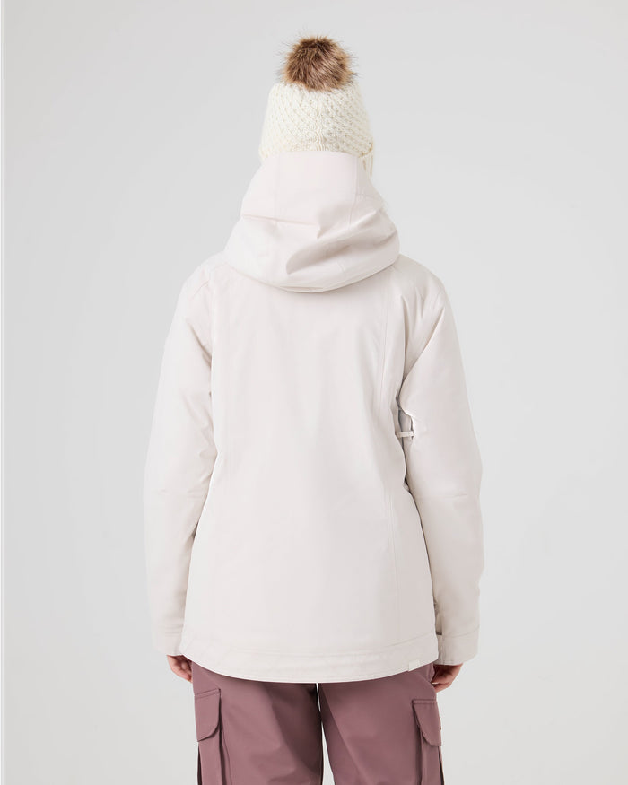 Wearing the Roxy Billie Jacket—a women’s snow jacket in white from Roxy—paired with a white knit beanie topped with a brown pom-pom and mauve pants, the person stands with their back to the camera against a plain backdrop.