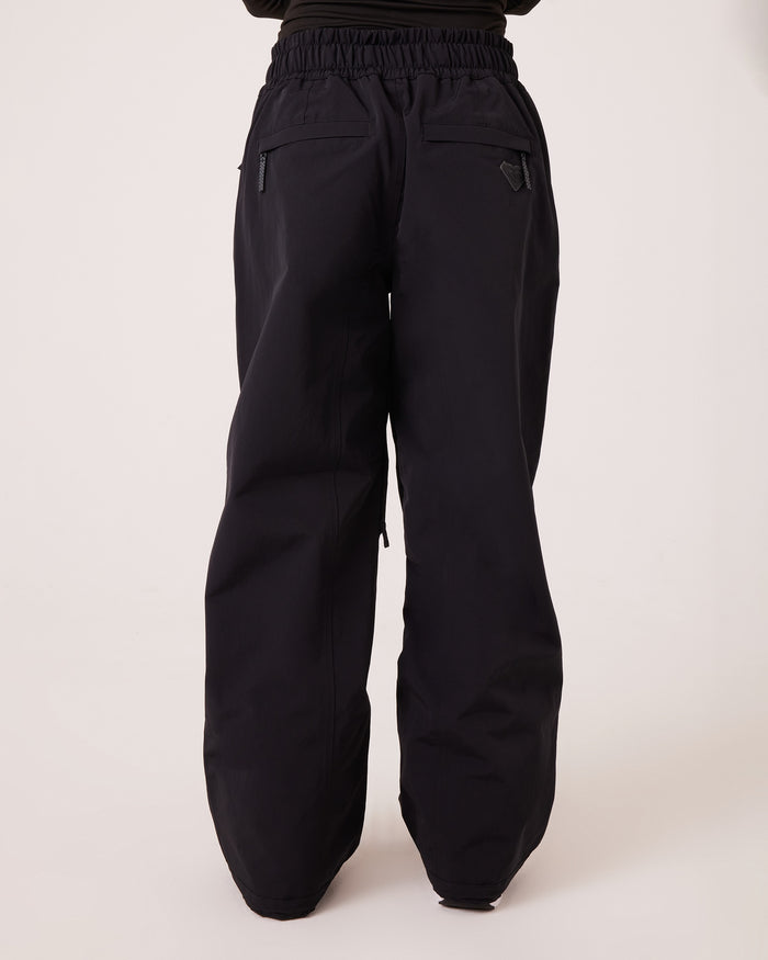 Back view of a person wearing Roxy Bleeker Pants—loose-fitting black women’s snowboard pants with an elastic waistband and two zippered back pockets. These pants feature a waterproof-breathable, PFAS-free design and are shown against a plain light background.
