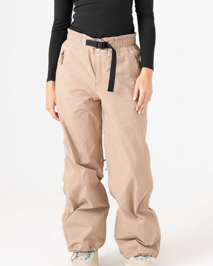 A person models the Roxy Bleeker Pants, styled with a black belt, a long-sleeved black top, and white shoes against a plain white background. Their face is not visible in the image.