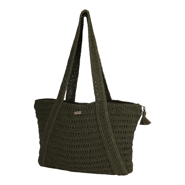 The Roxy Chips And Guac Tote Bag is a dark green crocheted tote featuring double handles, a zippered top closure with a small tassel attached, and a small rectangular metal logo plate on the front. Set against a plain white background, this spacious bag is the perfect travel companion for your everyday adventures.