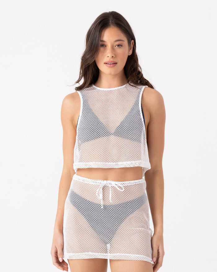 A woman poses against a white background in the Roxy Don't Mesh With Me Crop Top Cover Up in Egret, styled over a black bikini with its matching high-waisted loose-fit mesh skirt featuring a drawstring.