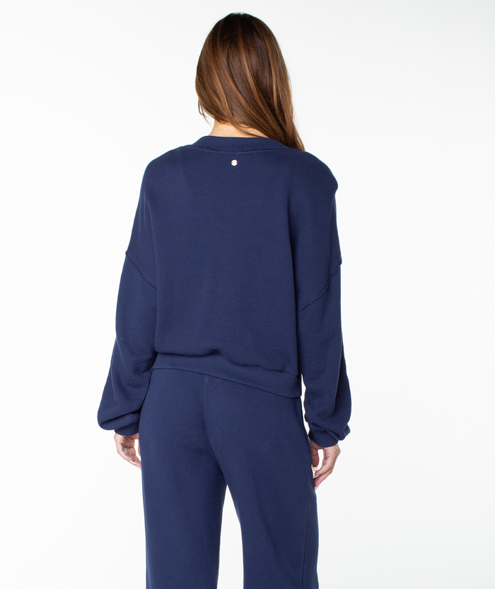 A person with long brown hair is shown from behind, wearing the Roxy Dream Thing Top, a navy blue cotton crewneck sweatshirt, against a plain white background.