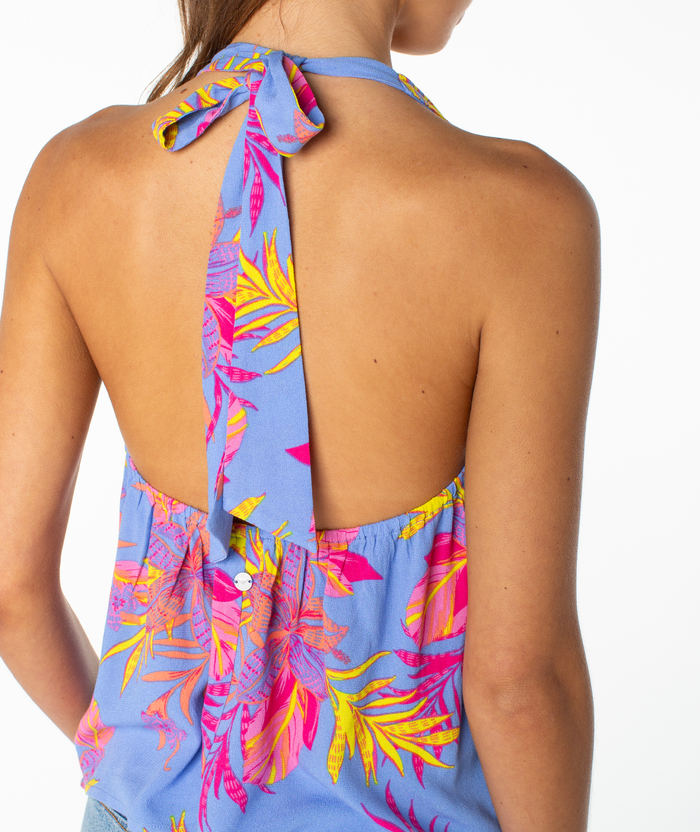 A person wears the Roxy Fairweather Top—a blue halter with a pink and yellow tropical floral print, tied at the neck in retro beachwear style, featuring an open back and baring part of the arm and shoulder.