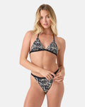 A woman with long blonde hair models the Roxy Geo Flower Fixed Triangle Bikini Top in a black/ivory print, standing against a plain white background and looking at the camera.
