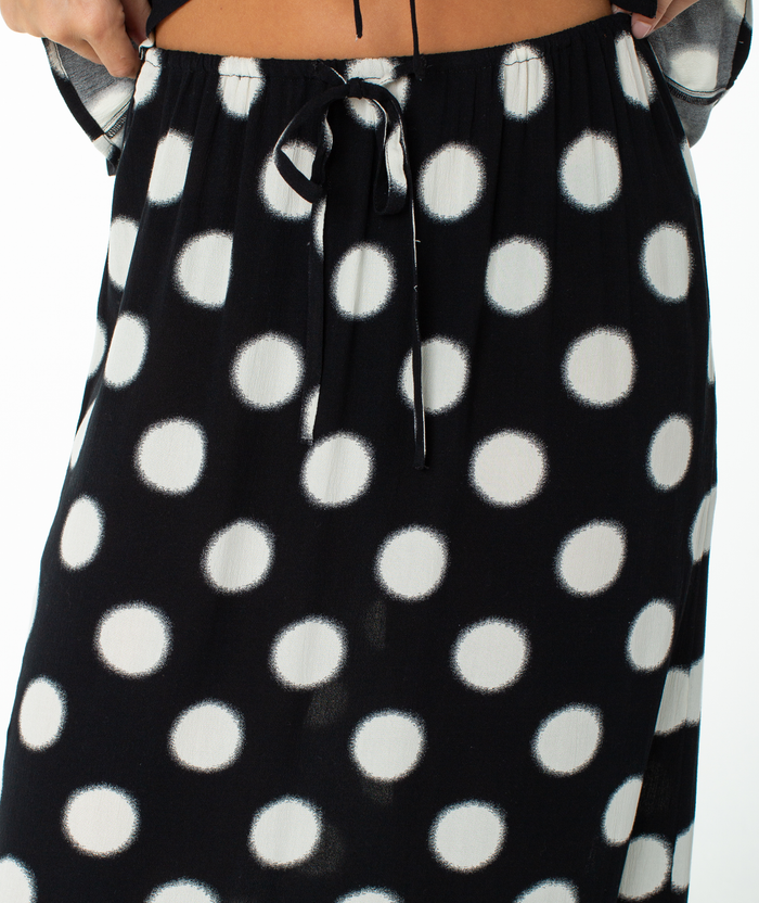 A close-up of the Roxy Iyla Skirt, featuring large white polka dots and a waist tie, worn by a person with their hands resting on their hips.