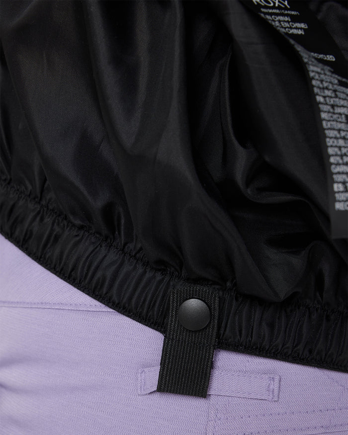 Close-up of the Roxy Jetty Jacket’s elastic waistband with a snap button detail, crafted from recycled materials and worn over light purple pants.