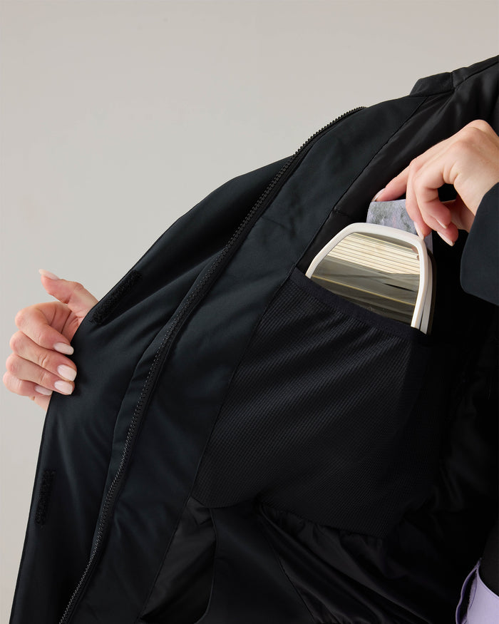 A person places a small, light-colored clutch bag into an inner mesh pocket of the Roxy Jetty Jacket—a women’s snowboard jacket crafted with recycled materials for warmth and sustainability.