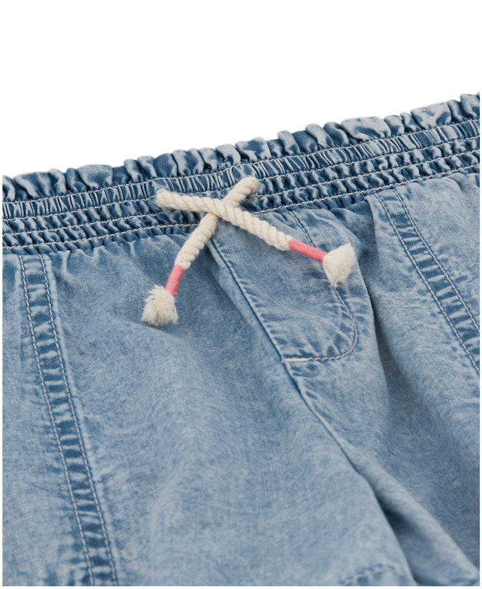 The Roxy Little Girls' Soleil Short features a light blue acid wash, smocked elastic waistband, front pockets, and a white rope drawstring with pink-accented ends.