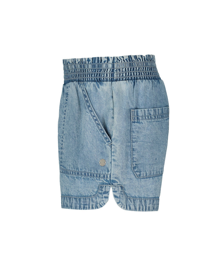 The Roxy Little Girls' Soleil Short features light blue lightweight denim, a smocked elastic waistband, front pockets, a decorative metal button, a back patch pocket, and gathered hems. Displayed on a white background.
