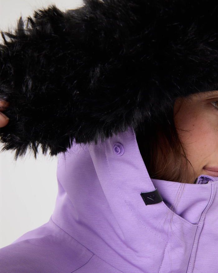 Close-up of a person wearing the Roxy Meade Jacket in lavender, featuring a black faux fur hood partially obscuring their face. Only one eye and part of their hand adjusting the hood are visible, drawing attention to the jacket’s tailored fit and 10K protection for warmth and style.