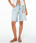 A person wearing Roxy's Message In A Bottle Short in light blue with frayed edges, paired with a white sleeveless top with rope tie and drawstring waist, plus brown sandals, stands against a white background.