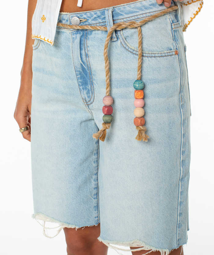 Wearing Roxy’s light blue Message In A Bottle Short with raw hems and a beaded drawstring waist, paired with a white shirt that has yellow stitching.