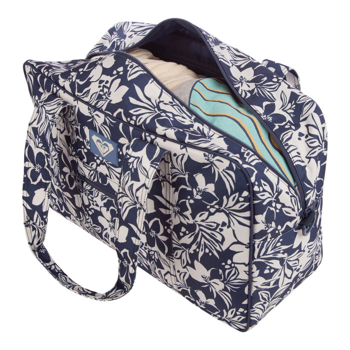 The Roxy Off Shore Duffel Bag in blue and white floral print is shown unzipped, displaying folded clothes inside, such as a cream sweater and a striped garment in shades of blue and green.