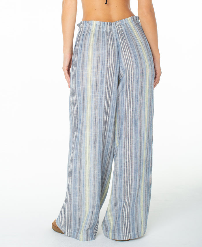 A person is shown from the back wearing the Roxy Offshore Pant—a pair of loose, wide-leg cotton pants in blue, gray, and yellow stripes. These vacation-ready pants feature an elastic waistband and a relaxed fit. The background is plain white.