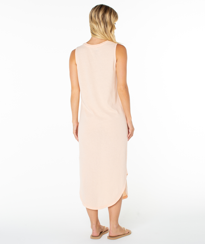 A woman with blonde hair faces away in the Roxy Peace Waves Wildflower Midi Dress in light peach, paired with beige flip-flops, against a plain white background.