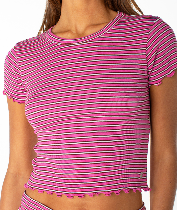 A person wearing the Roxy Poolside Crop Tee—a pink and white, short-sleeve ribbed top with horizontal stripes and ruffled edges—perfect for a relaxed summer look.