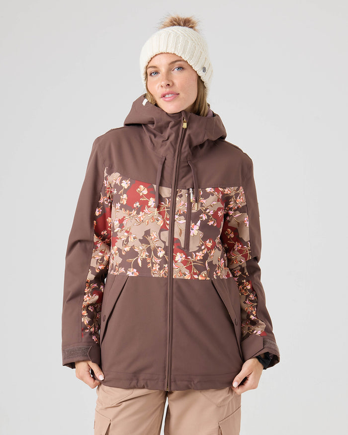 A person wearing a Roxy Presence Parka Jacket in Shopping Bag, light brown pants, and a white knit beanie with a pom-pom stands facing forward against a plain light background.