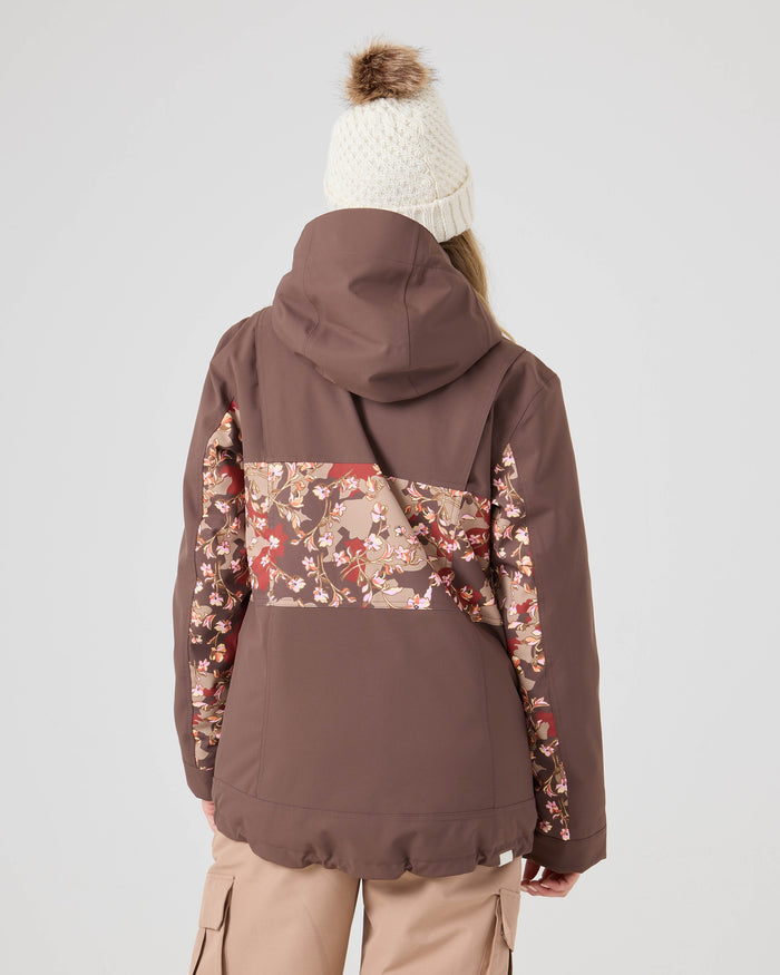 A person wearing a knitted white beanie and beige cargo pants stands facing away, showcasing the details of the Roxy Presence Parka Jacket—a women’s snowboard jacket featuring a brown colorway with a floral panel across the back.