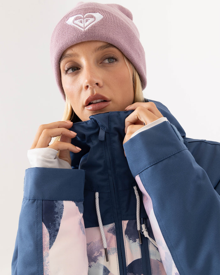 A woman in a light purple beanie and blue Roxy Presence Parka Jacket zips up her coat. She looks slightly to the side with a neutral expression, set against a plain white background.