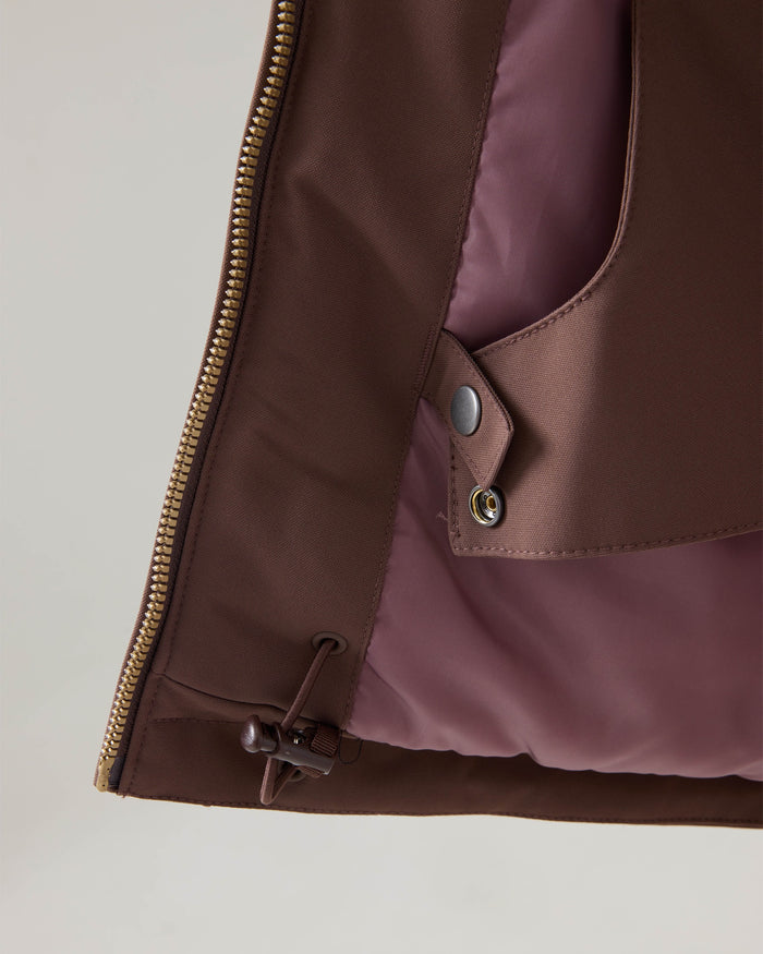 Close-up of the Roxy Presence Parka Jacket in brown, showcasing a brass zipper, snap button tab, and drawstring toggle at the hem. The inner lining is a contrasting mauve color.