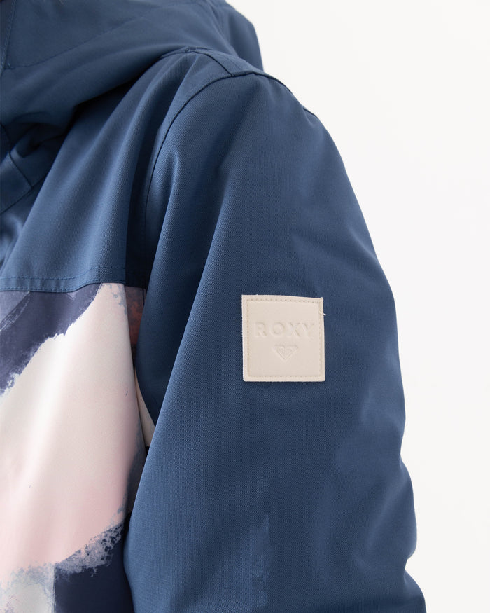 Close-up of a blue Presence Parka Jacket sleeve by Roxy, showcasing a white square patch embossed with the ROXY name and heart logo. This women’s snow jacket offers 15K protection for enhanced performance and features a colorful, abstract design across part of the chest.