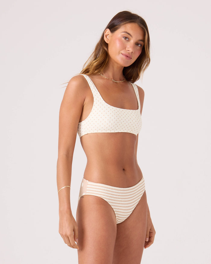 A woman with long brown hair and a neutral expression stands against a plain background wearing the Roxy Polka Dots Hipster Full Bikini Bottom. The bikini bottom features a subtle dot pattern and provides full coverage.
