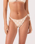 A woman wears the Roxy Polka Dots Tie Side Cheeky Bikini Bottom in Neutral Combo with a matching top, standing against a plain background.