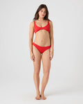 A woman stands barefoot against a plain white background, wearing a matching red bikini featuring the Roxy Rib Roxy Love Hipster Moderate Bikini Bottom. She faces forward with a neutral expression and her arms relaxed at her sides.