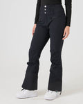 A person is shown from the waist down wearing Roxy’s Rising High Pants in black—high-waisted women’s snow pants featuring front buttons, zippered pockets, and 15K/15K protection—paired with white sneakers, against a plain light background. Their upper body is cropped out of the image.