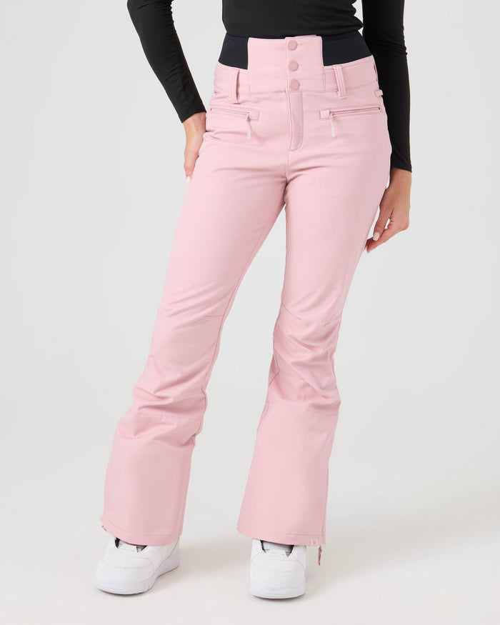 Wearing the Roxy Rising High Pants in light pink, paired with a black long-sleeve top and white sneakers, a person stands against a plain light background.