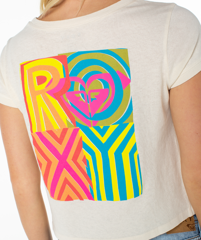 A person wears the Roxy Echo Tee by Roxy—a white shirt with bold, colorful geometric "ROXY" lettering and a heart logo on the upper back. The breezy fit and playful design make it a perfect summer staple. Only the upper back and arm are shown.
