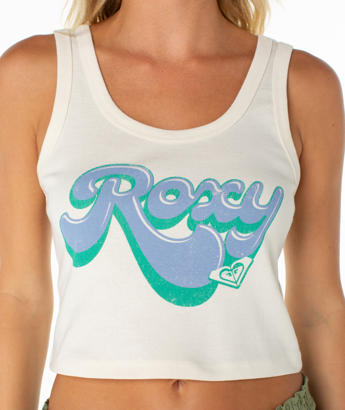 A person, with only their torso visible, wears the Roxy Scoop Baby Rib Tank—a white, cropped summer essential in soft cotton with "Roxy" printed in bold blue and green letters across the front.