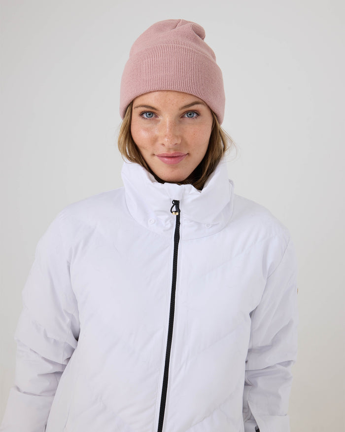 A person wearing a pink knit beanie and the Roxy Snowdrift Jacket, a women’s ski jacket featuring cozy faux-down insulation, stands against a plain light background and looks directly at the camera with a slight smile.