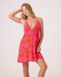 A woman with long blonde hair and a gold necklace models the Roxy Sun Chasers Plunge Dress Cover Up in Pink Combo, featuring a sleeveless V-neck design with thin straps and crinkle rayon fabric, set against a plain light background.