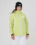 A woman stands against a plain light background, dressed in the Roxy Zephyr Jacket in Lily Green with white zippers, paired with white pants and a black beanie featuring a white logo. This technical outerwear is ideal for ski and snowboard enthusiasts who value both style and functionality.