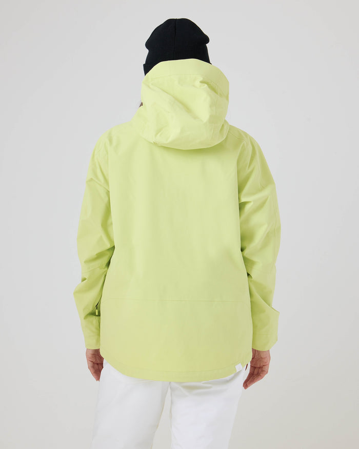 A person is seen from behind, standing against a plain white background, wearing the Roxy Zephyr Jacket in light green with the hood up, paired with white pants and a black beanie.
