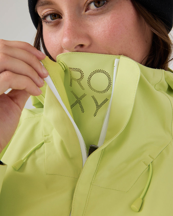 A person in a lime green Roxy Zephyr Jacket partially unzips the technical outerwear, revealing the ROXY branding inside. Ideal for ski and snowboard adventures, the standout jacket is paired with a black beanie, with only the lower half of their face visible.