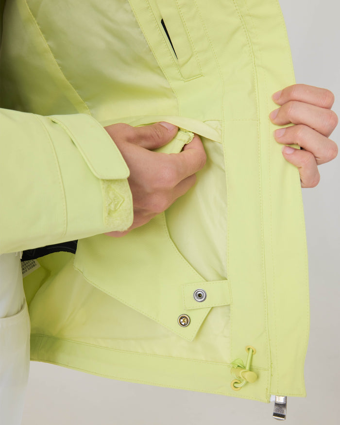 A person opens a light yellow Roxy Zephyr Jacket, revealing the inside pocket and snap buttons—showcasing the thoughtful details typical of technical outerwear designed for ski and snowboard enthusiasts.